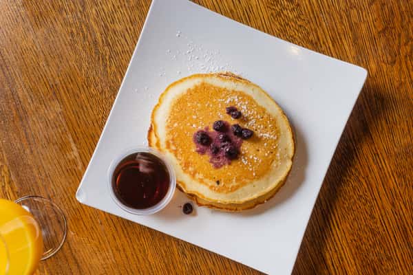 Overhead view of fluffy pancakes topped with blueberries and served with warm maple syrup.