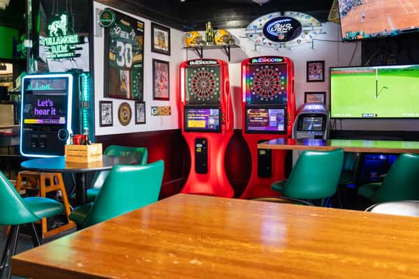 Game room area with dart boards, sports memorabilia, and large-screen TVs inside a vibrant sports lounge.