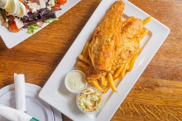 Overhead view of crispy fish and chips served with fries, tartar sauce, and classic pub-style sides.