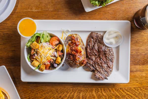 Steak dinner special featuring grilled steak, loaded baked potato, vegetables, and garlic bread.