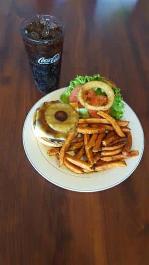 Cheeseburger with pineapple, onion ring, lettuce, and tomato with a side of fries