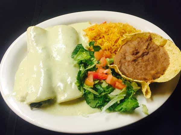 2 burritos covered in a cream sauce with a side of rice, refried beans and vegetables