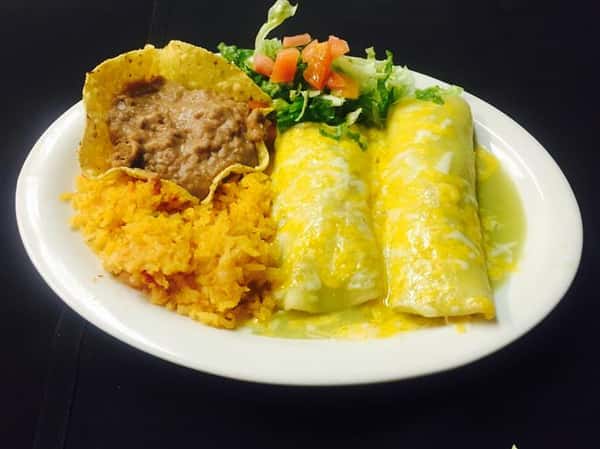 2 burritos covered in cheese with a side of rice, refried beans and vegetables