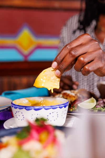 Close-up of a tortilla chip being dipped into creamy queso blanco in a hand-painted Mexican bowl.