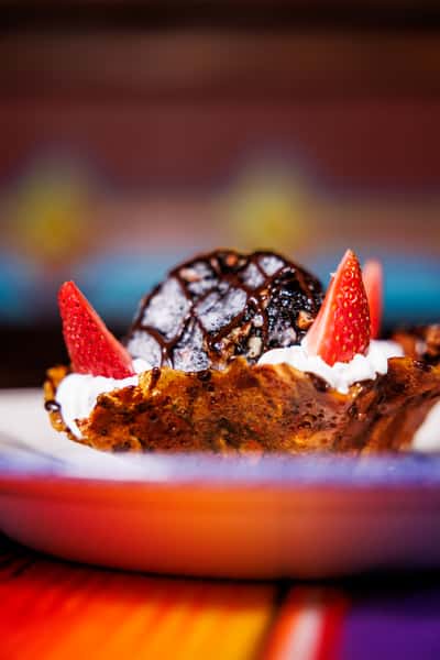 Decadent fried ice cream dessert served in a crispy cinnamon shell, topped with a drizzle of chocolate syrup, fresh strawberries, and whipped cream—perfect for a festive Mexican dining experience.