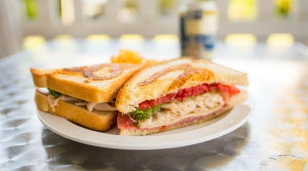 Toasted club sandwich with turkey, salami, cheese, lettuce, and tomato, served with chips on a white plate.