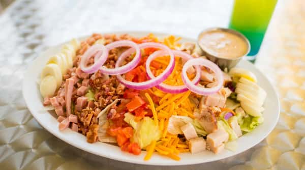 Chef salad with ham, bacon, egg slices, cheese, chicken, tomatoes, red onion, and dressing.