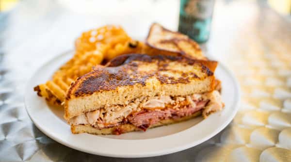 Grilled sandwich with turkey and ham, served with waffle fries on a white plate.