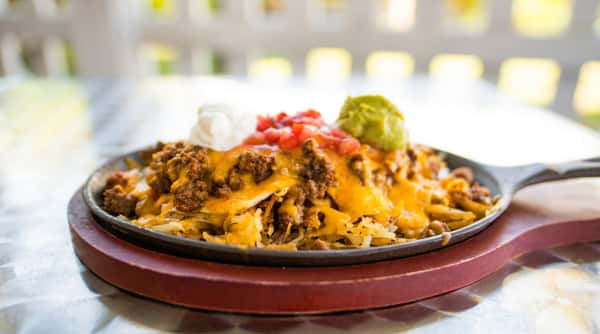 Skillet nachos with ground beef, melted cheese, sour cream, diced tomatoes, and guacamole.