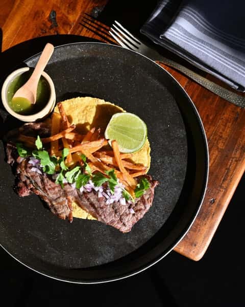 Top view meat dish with garnish and a side of sauce
