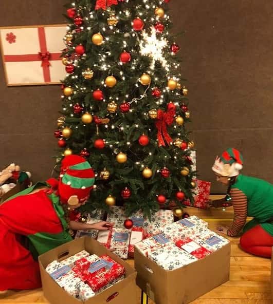 two people placing gifts under a christmas tree