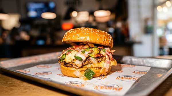 A large burger with melted cheese, bacon, and sliced green peppers on a sesame seed bun.