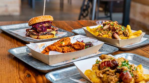 A spread of fast food dishes: a burger with melted cheese and red onions, chicken tenders, and loaded fries.