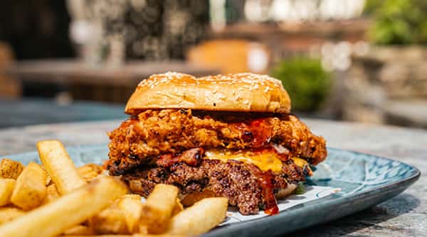 Double patty burger with fried chicken, melted cheese, bacon, and fries.
