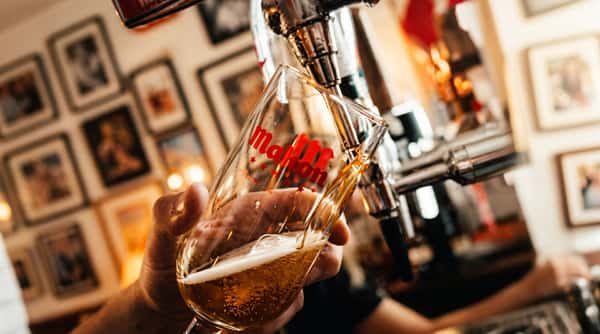 A clear glass with "Molson" in red being filled with amber beer from a tap, held by a hand.