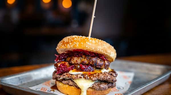 Double cheeseburger with two patties, melted cheese, and a dark red relish, served on a sesame seed bun.