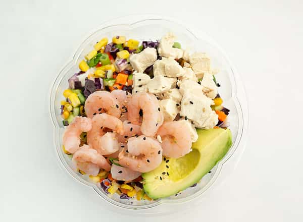 Here's a top-down shot of a customizable poke bowl. It features corn, purple cabbage, tofu, shrimp, and half an avocado, seasoned with sesame seeds.
