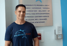 The image shows a man in front of an Atlantic Poké logo and mission statement. "Our mission is to provide a great customer experience through consistent delivery of flavorful food with exceptional and friendly customer service in a clean, well designed, inviting atmosphere."