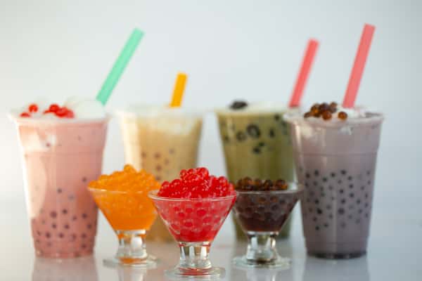 A photo shows a variety of bubble teas with colorful straws. Small glasses hold extra tapioca pearls in orange, red, and brown.