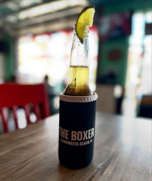 Ice-cold bottled beer with a fresh lime wedge in a branded koozie at The Boxer Kitchen & Bar in Clearwater Beach.