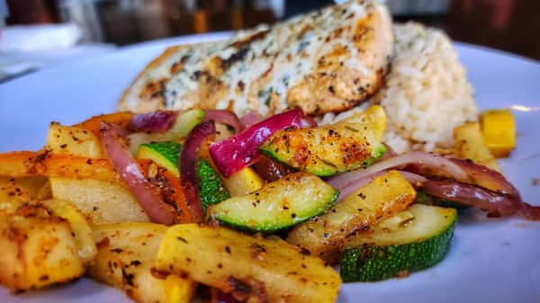 Grilled chicken breast served with seasoned rice and sautéed zucchini, squash, and red onions for a fresh, flavorful entrée.