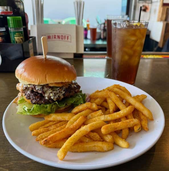 Juicy cheeseburger with fresh lettuce and crispy onion straws, served with seasoned French fries and an iced beverage.