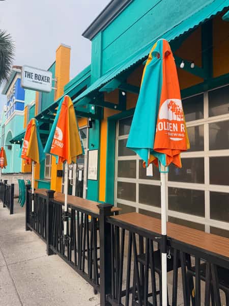 Colorful exterior of The Boxer Kitchen & Bar with sidewalk patio seating, vibrant coastal-inspired design, and casual dining ambiance.
