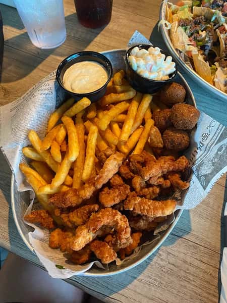 Fried shrimp basket served with seasoned French fries, hush puppies, coleslaw, and creamy dipping sauce for a classic seafood meal.