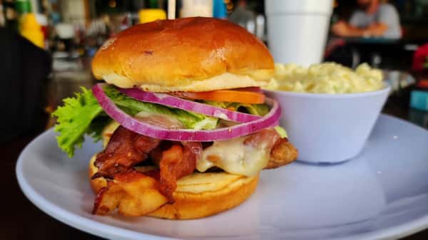 Bacon cheeseburger stacked with crispy bacon, melted cheese, fresh lettuce, tomato, red onion, and pickles on a toasted brioche bun, served with a side of creamy coleslaw.