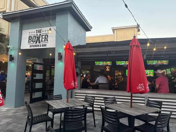 Exterior view of The Boxer Kitchen & Bar featuring outdoor patio seating, string lights, and an open-air sports bar atmosphere.