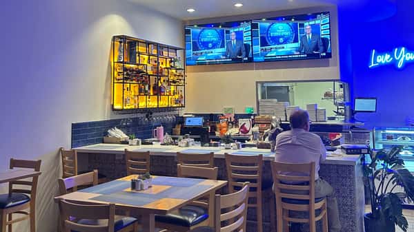 Restaurant dining area with bar seating, wall-mounted TVs, and wooden tables.