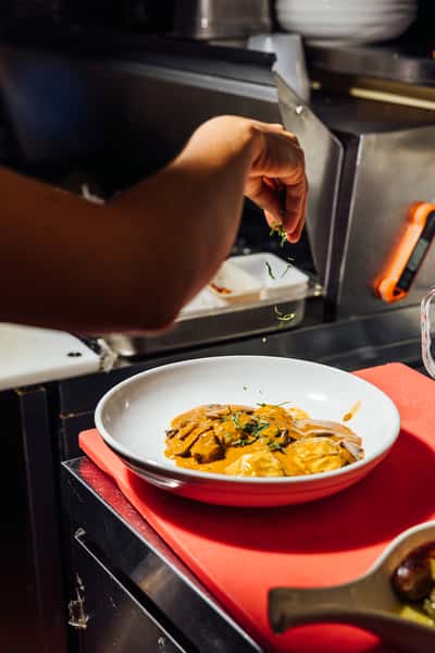 Chef garnishing a rich mushroom and cream pasta with fresh herbs in a kitchen, emphasizing handcrafted Italian cuisine detail.