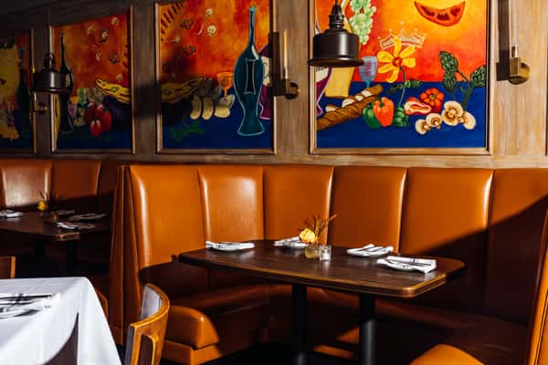 Cozy Italian restaurant booth seating with tan leather banquettes and colorful painted murals above, set for service with white napkins and table settings.