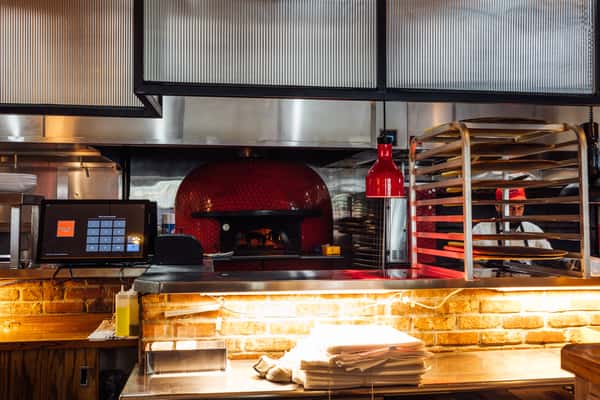 Open kitchen pizza station featuring a wood‑fired oven, prep counter, and chef working behind the scenes—ideal for showcasing authentic pizza preparation in an Italian restaurant kitchen.