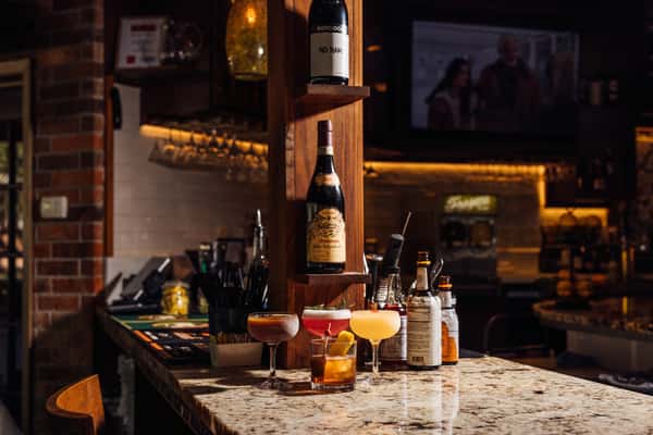 Elegant bar setup with a variety of colorful cocktails displayed on a marble countertop alongside wine bottles and bitters.