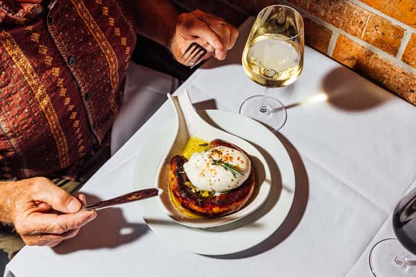 Diners table scene with grilled sausage topped with burrata and a glass of white wine, capturing a relaxed Italian dining moment.