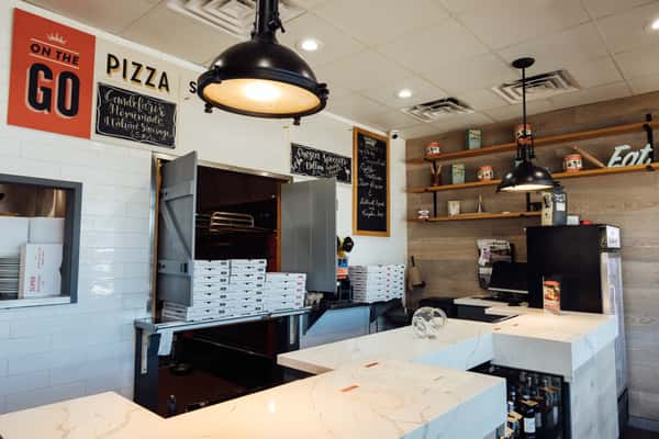 Casual pizza pickup counter with stacks of pizza boxes, chalkboard menu signage, and marble countertop—ideal for highlighting convenient on‑the‑go Italian pizza service.