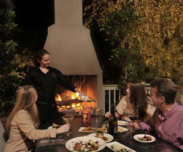 outdoor fireplace with table and 3 people sitting in the chairs looking at the waitress