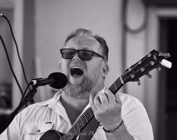 Scott Gronsky playing guitar and singing into a mic.