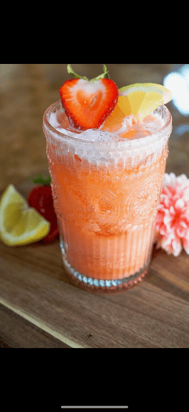 Refreshing strawberry lemonade served over ice in a decorative glass, garnished with fresh strawberry and lemon slices.