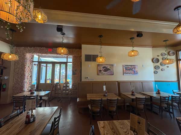 Cozy dining area with wood tables, woven pendant lights, floral entryway, and colorful wall decor in a vibrant Mexican restaurant.