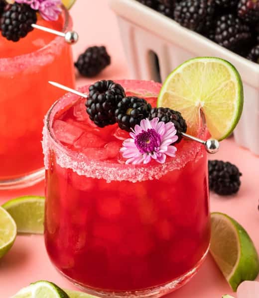 Blackberry margarita with a sugar rim, garnished with fresh blackberries, lime slice, and a purple edible flower.