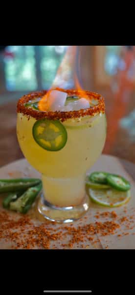 Spicy flaming margarita garnished with jalapeño slices, lime, Tajín rim, and ice, served in a chilled goblet glass.