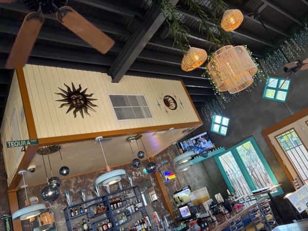 Eclectic bar area with hanging lights, disco balls, and sun decor, featuring a vibrant selection of bottles and teal-framed windows.