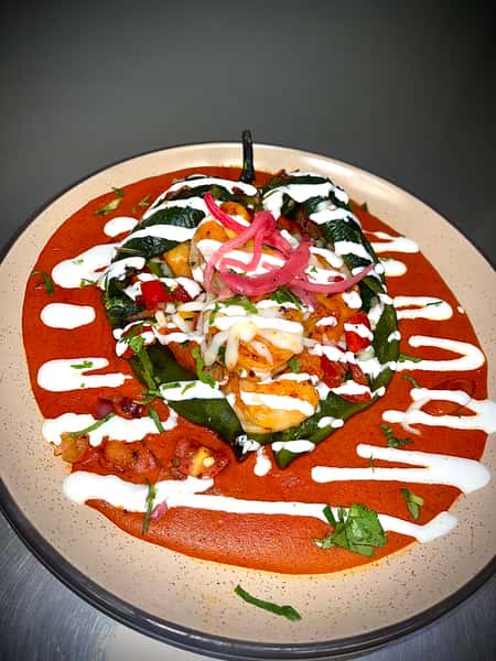 Stuffed poblano pepper topped with sautéed shrimp, onions, and crema over a bed of rich red sauce, garnished with fresh herbs.