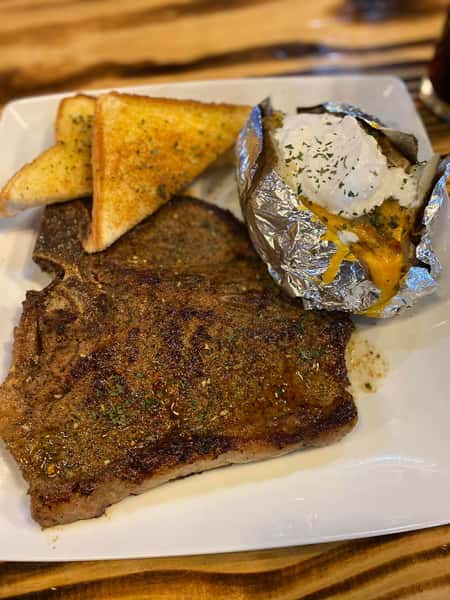 Grilled T-bone steak served with garlic toast and a loaded baked potato topped with sour cream, cheese, and herbs.