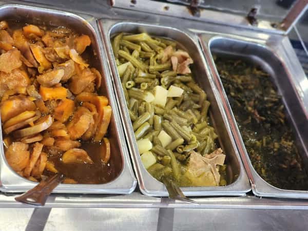 Hot food buffet featuring candied yams, green beans with potatoes and ham, and braised collard greens with smoked meat.