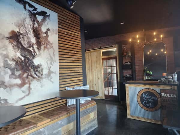 Cozy café interior with rustic wooden accents, a tufted bench, abstract wall art, and a warm chandelier above the counter.