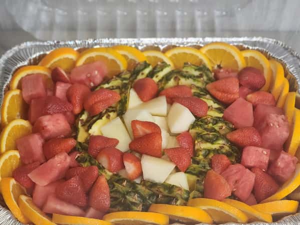 Colorful fruit tray with pineapple halves topped with strawberries, honeydew, watermelon, and a border of fresh orange slices.