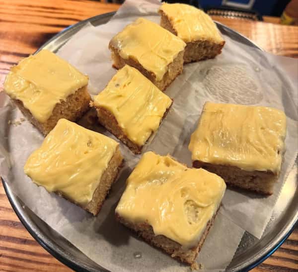 Banana cake squares topped with thick yellow frosting, arranged on parchment paper on a metal tray.